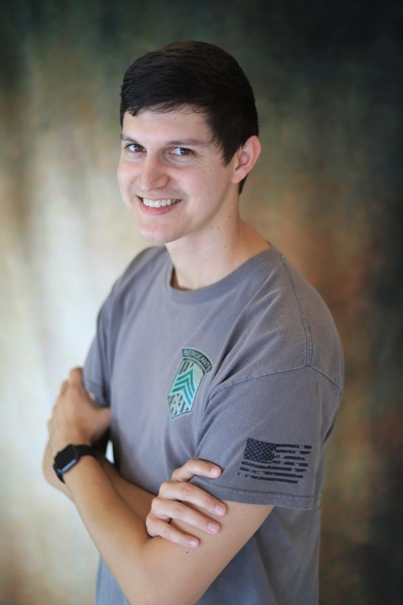 Person smiling with arms crossed, wearing a gray T-shirt against a blurred studio background