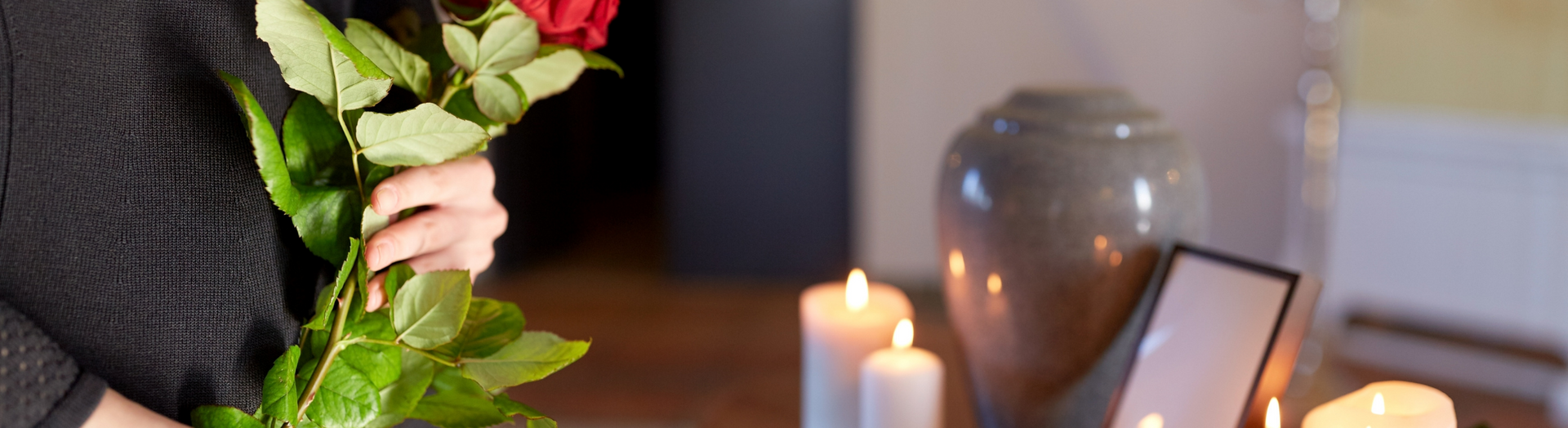 Hand holding red roses beside lit candles and a framed photo on a table