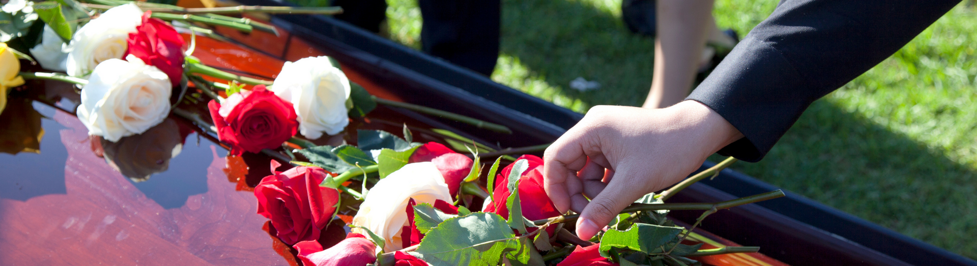 Hands placing red and white flowers on a casket at an outdoor funeral ceremony