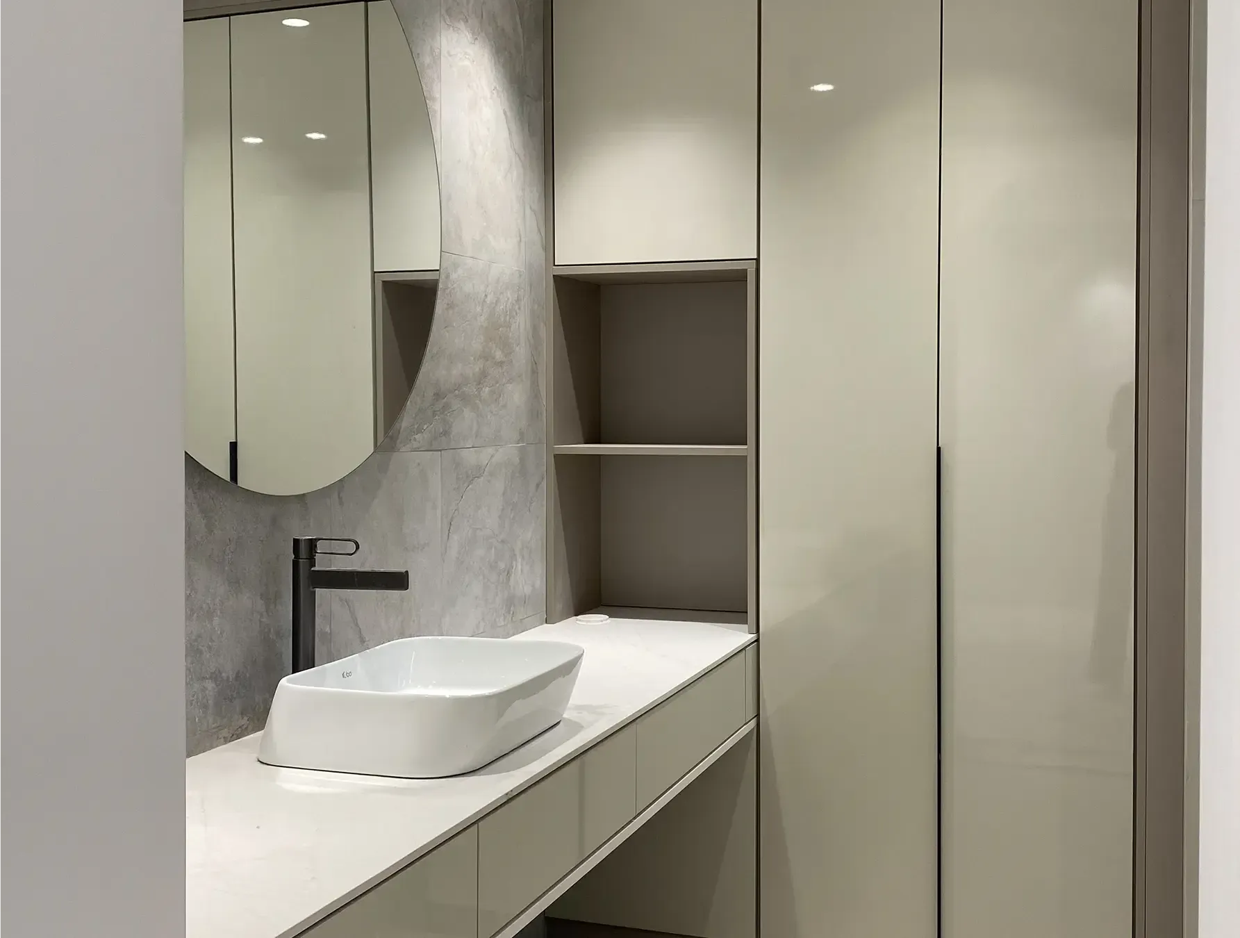 Mueble de baño moderno con lavabo blanco, grifo negro, espejo grande y estantes empotrados.
