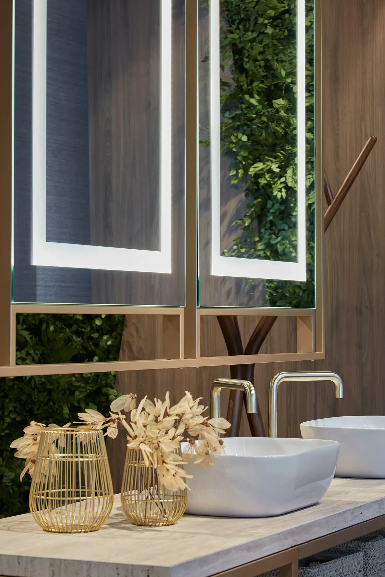 Tocador de baño moderno con lavabo blanco, decoración dorada y ventana abierta con vistas a la vegetación.