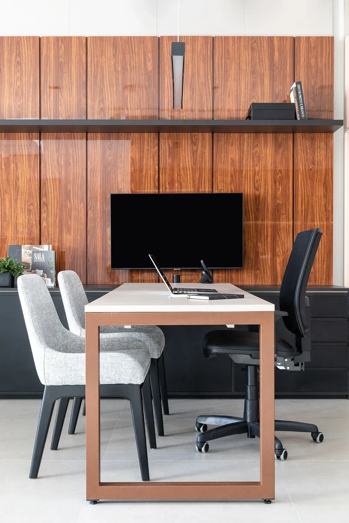 Sala de reuniones moderna con mesa, sillas, monitor de ordenador y pared revestida de paneles de madera.