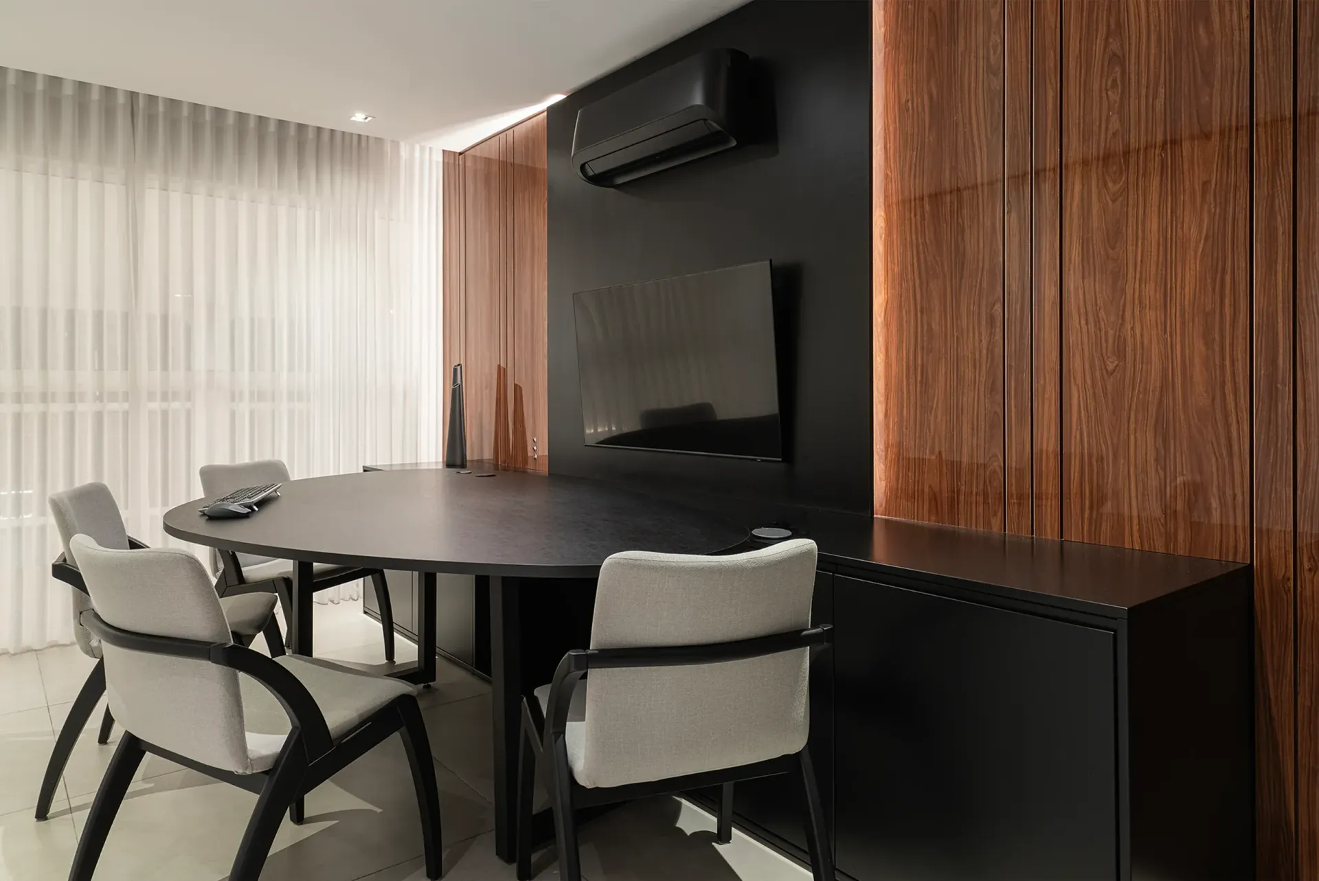 Comedor moderno con mesa redonda negra, sillas tapizadas, pared de madera y televisor montado en la pared.