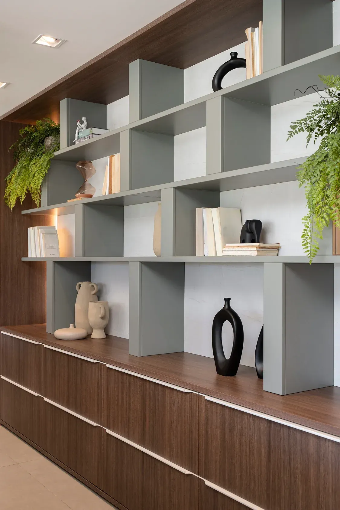 Estanterías modernas de color gris con jarrones decorativos, libros y plantas sobre armarios con paneles de madera.