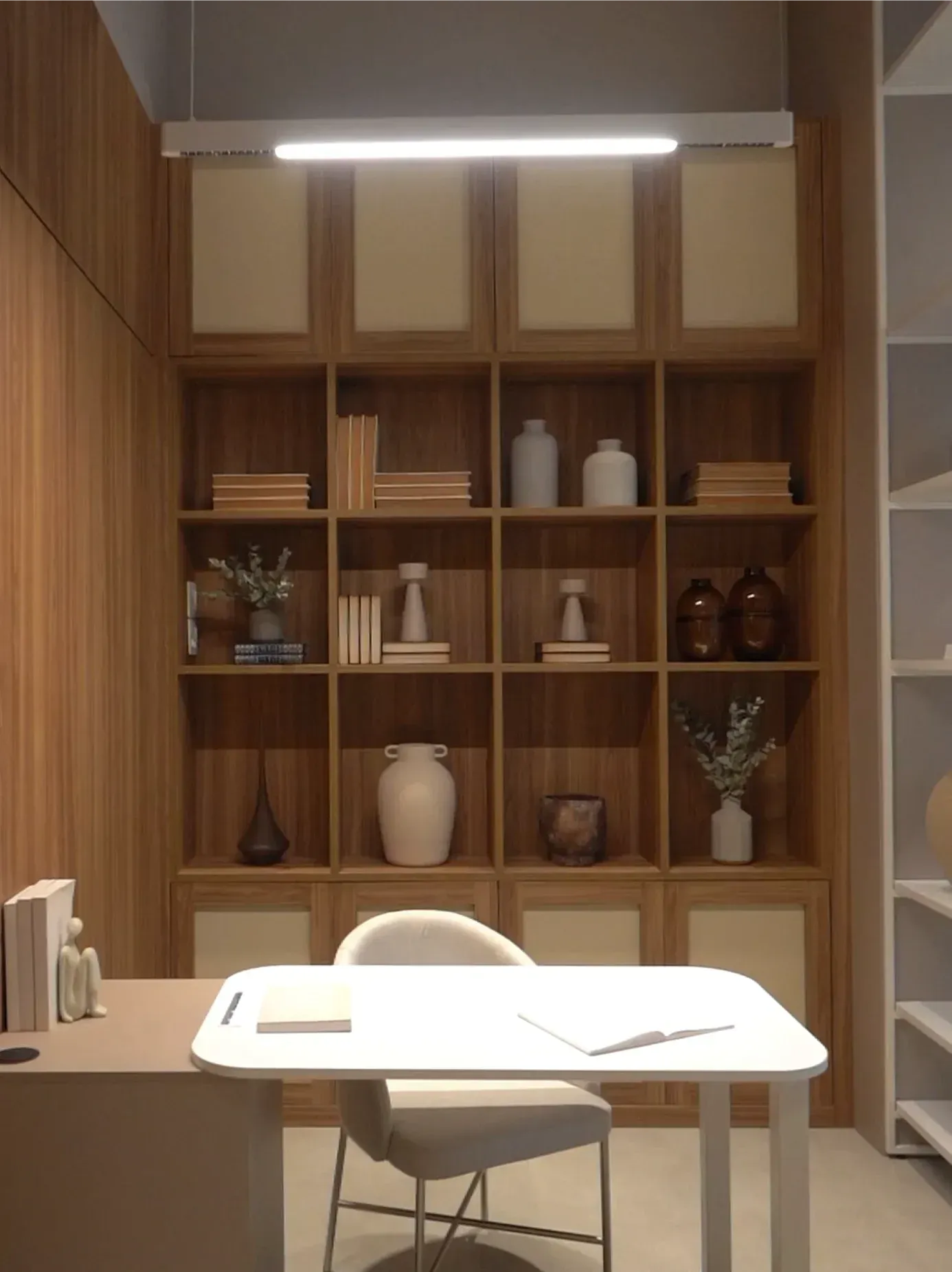 Acogedor rincón de oficina de madera con estantes, escritorio blanco, silla, libros y jarrones decorativos bajo una lámpara de techo.