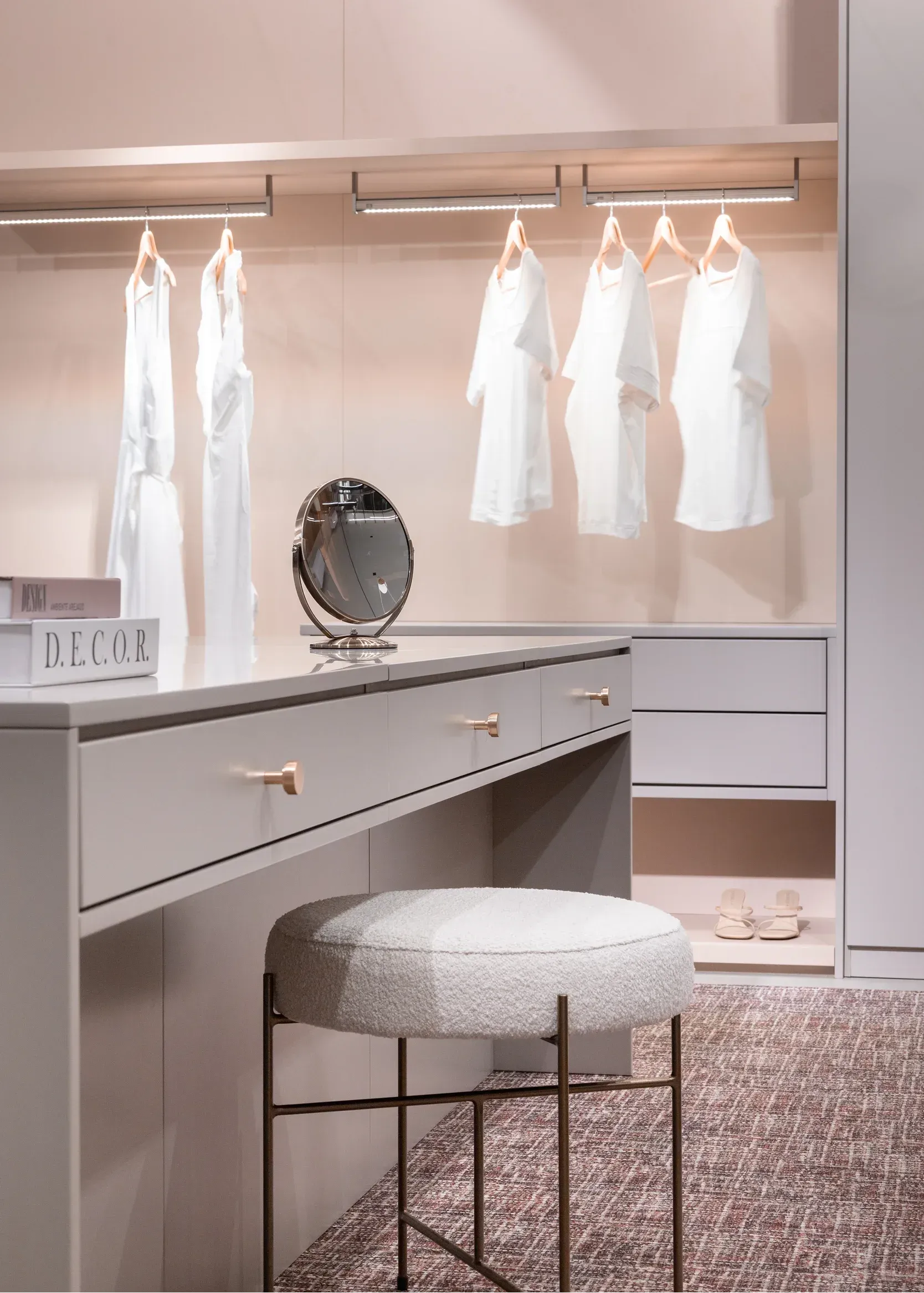 Vestidor moderno con percheros iluminados, espejo de tocador y taburete mullido.