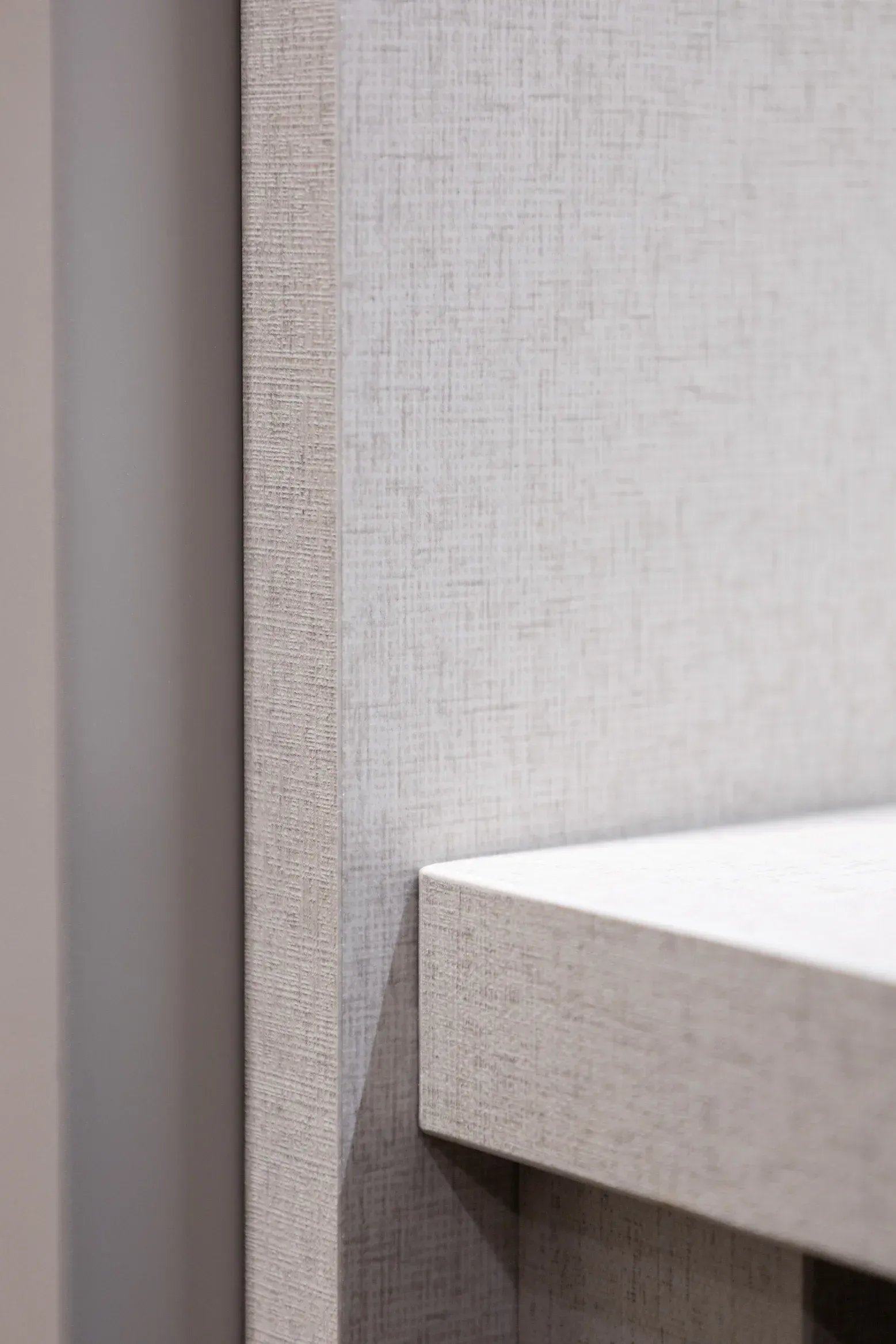 Primer plano de una estantería blanca contra una pared texturizada de color gris claro y un panel gris oscuro.