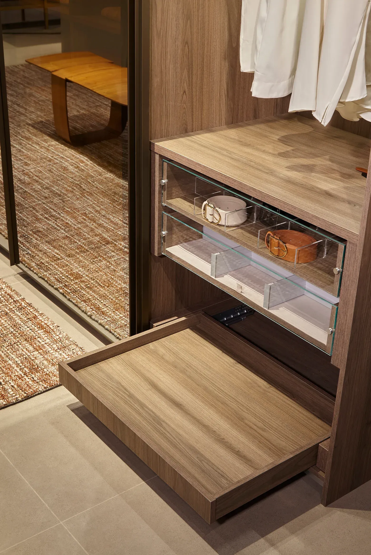 Closet abierto con estante extraíble para zapatos y cajones junto a una puerta con espejo en un vestidor con acabado de madera.