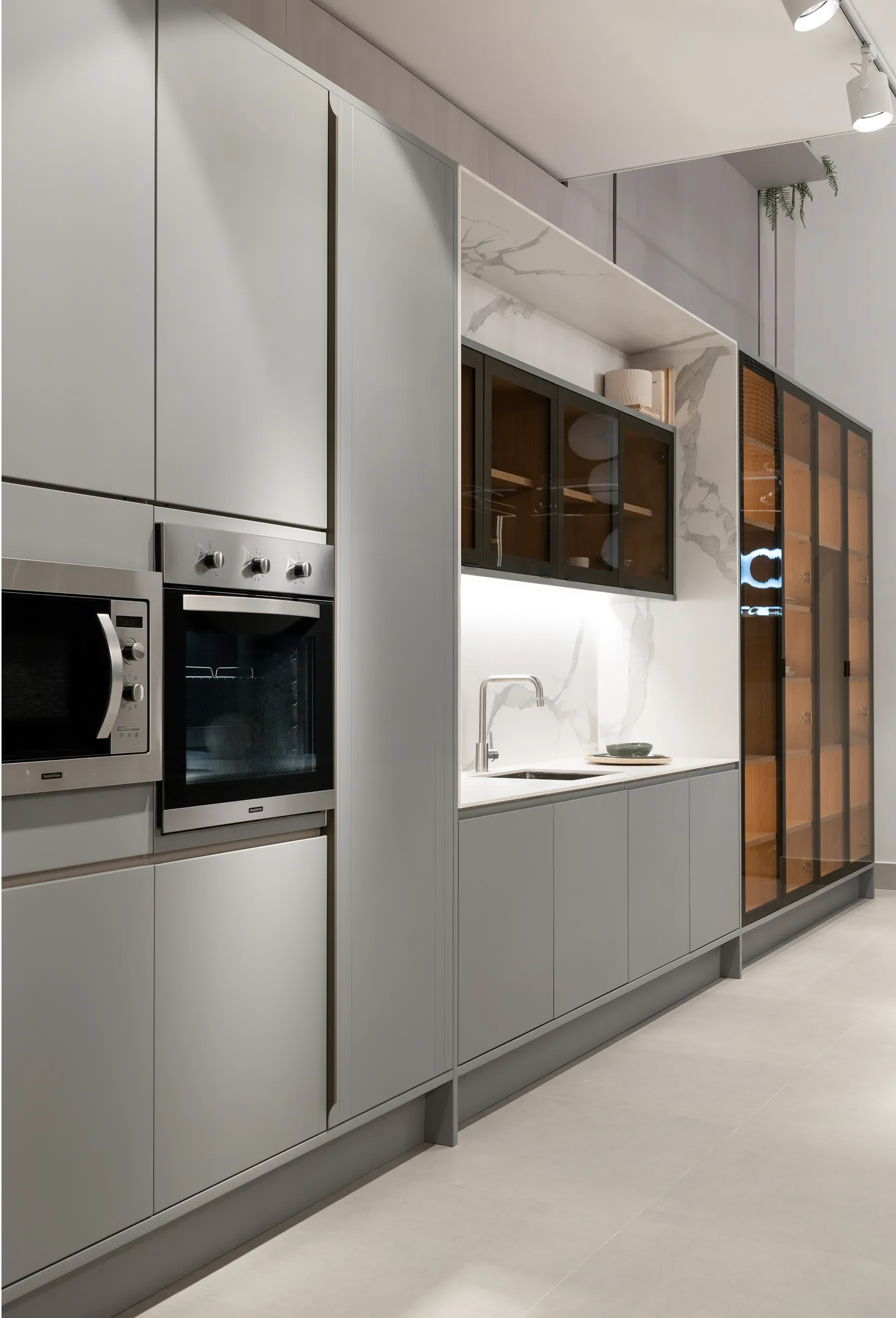 Sala de exposición de cocinas modernas con elegantes gabinetes grises, hornos empotrados y área de encimera blanca.