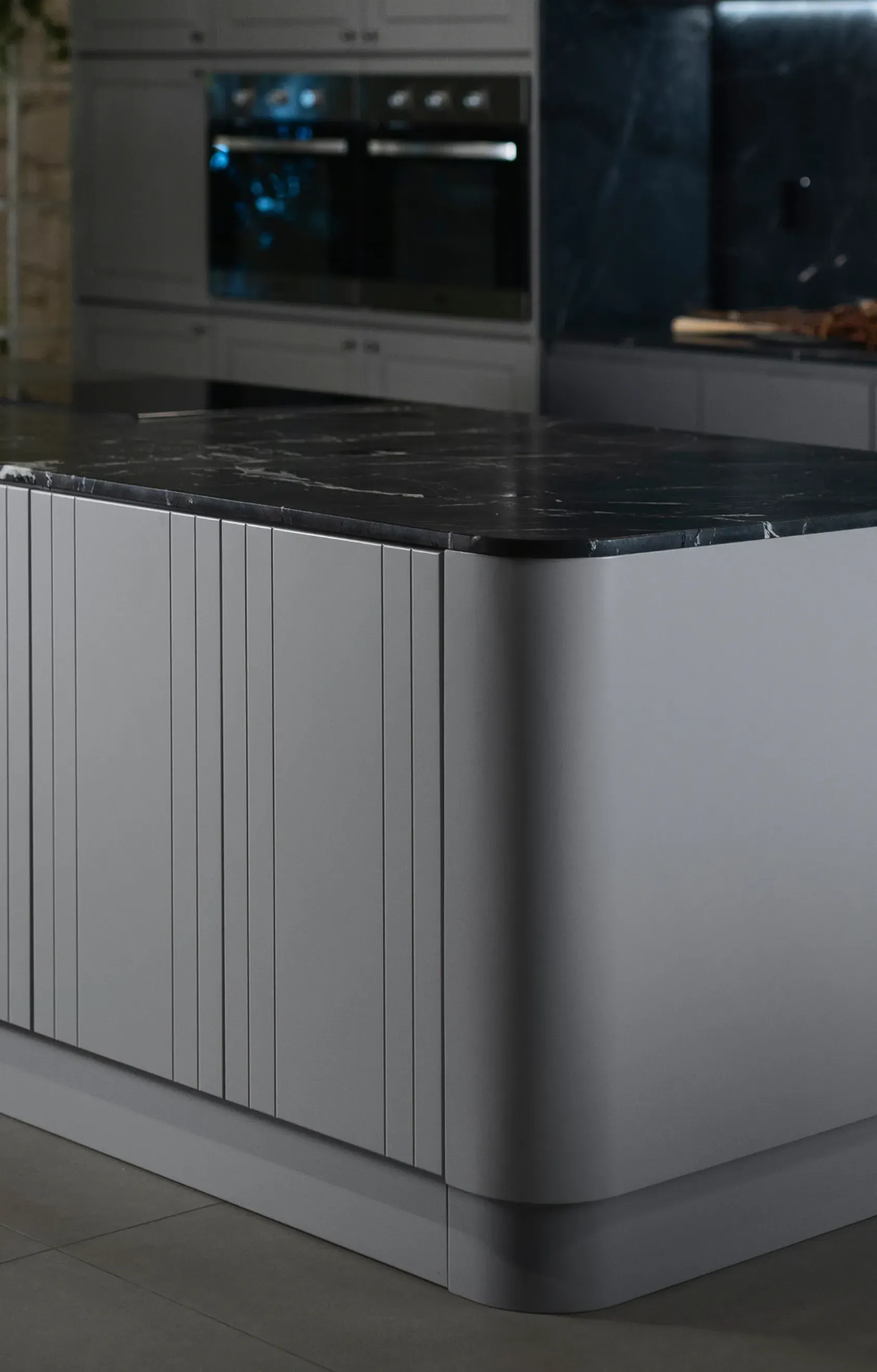 Isla de cocina moderna con gabinetes blancos y encimera de mármol negro, frente a electrodomésticos empotrados.