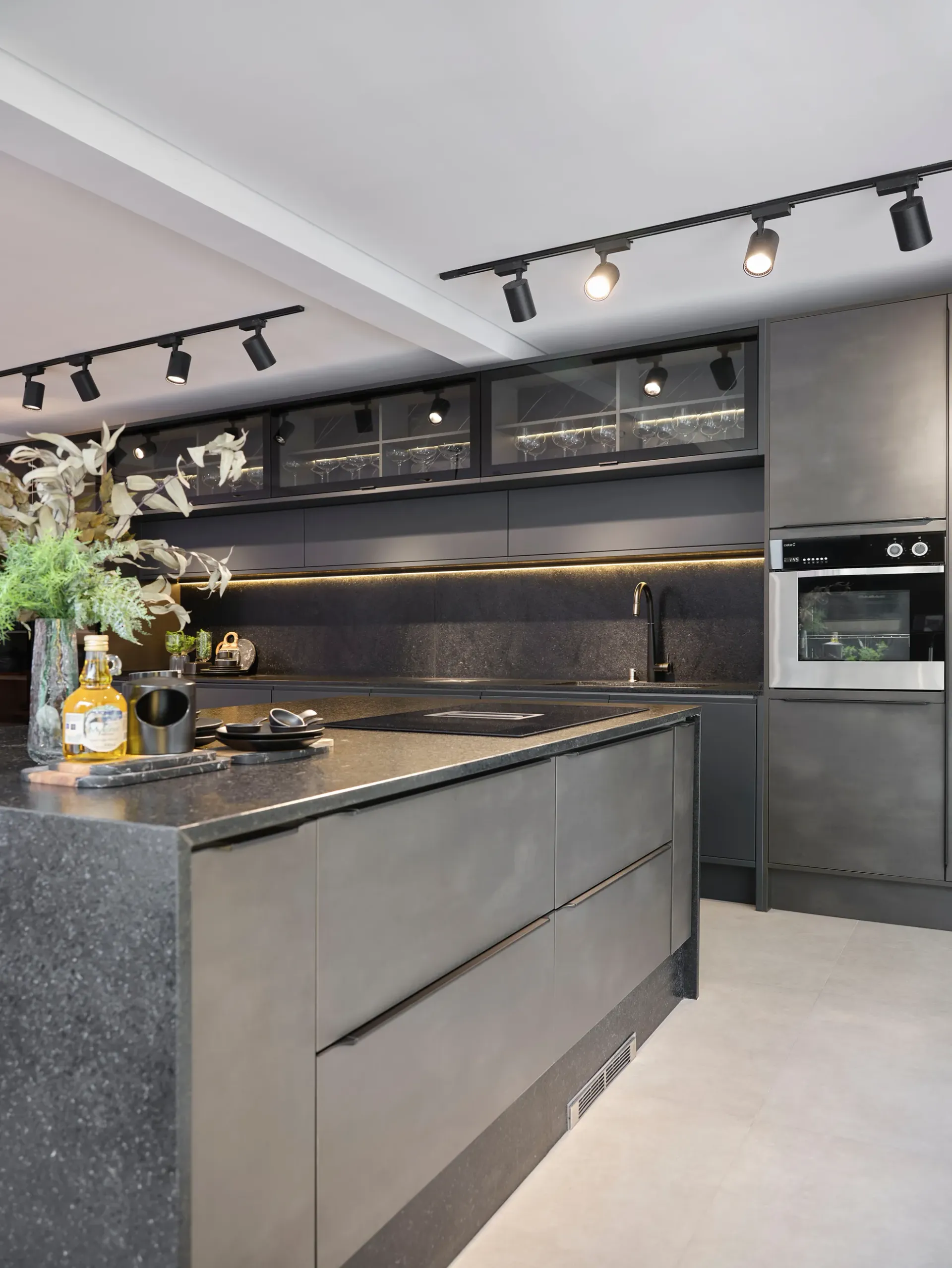 Cocina moderna de color gris con una gran isla, encimeras negras, iluminación empotrada y electrodomésticos integrados.