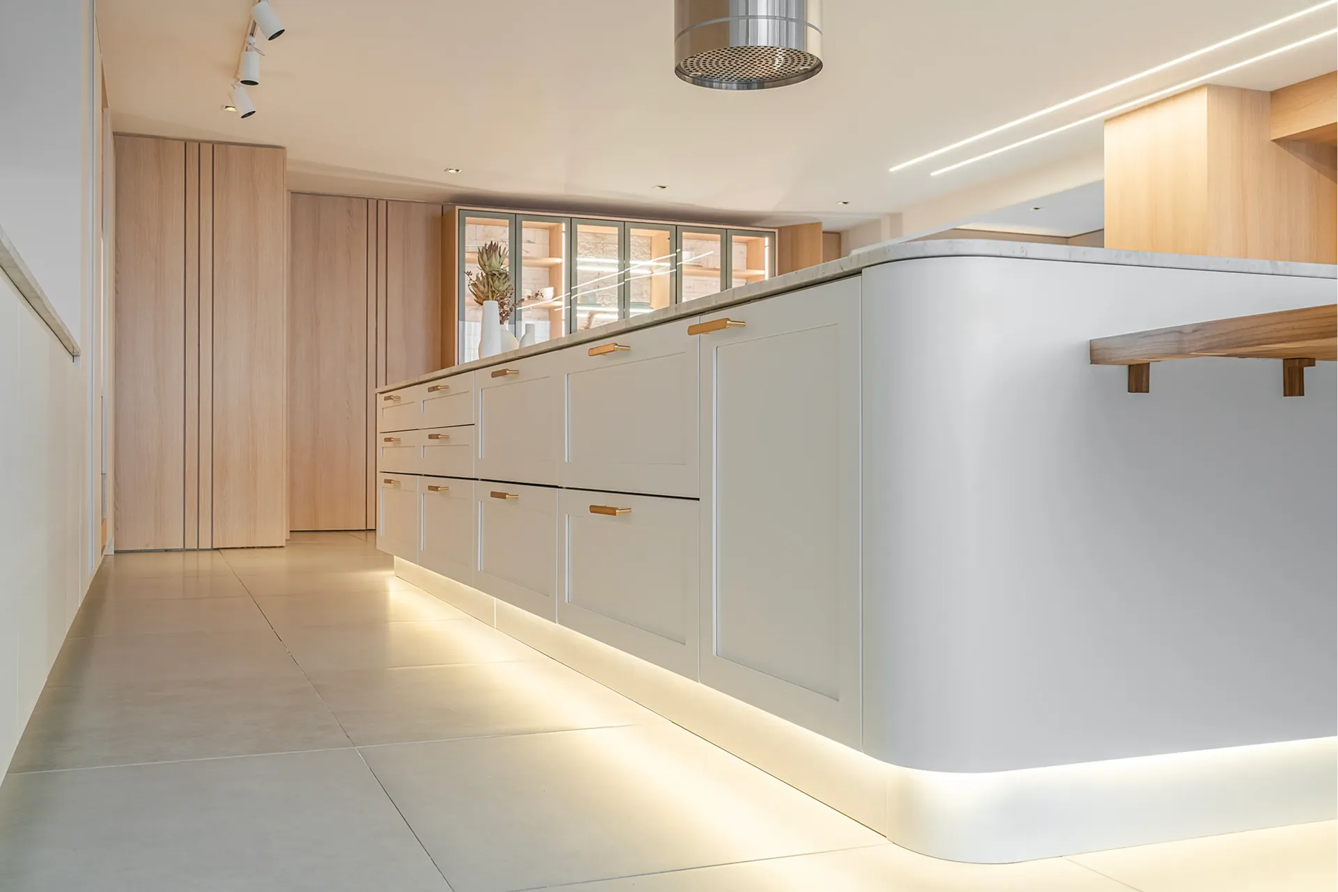 Cocina moderna minimalista con armarios de madera clara, isla blanca e iluminación tenue bajo los armarios.