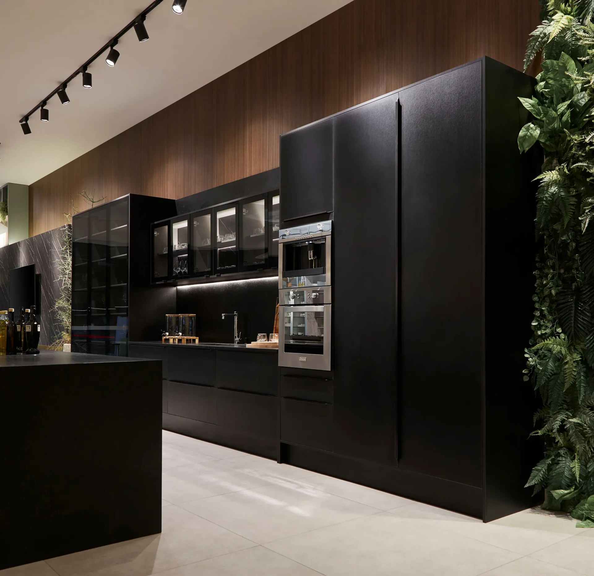 Cocina moderna con gabinetes en negro mate, electrodomésticos empotrados y pared revestida de madera cálida bajo iluminación de riel.