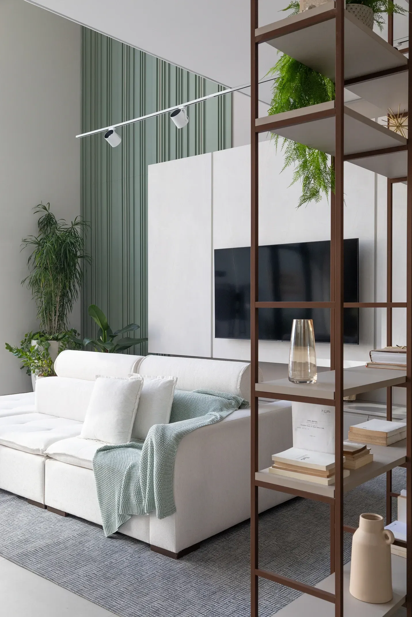 Sala de estar moderna con sofá blanco, plantas y separador de ambientes con estanterías de madera.