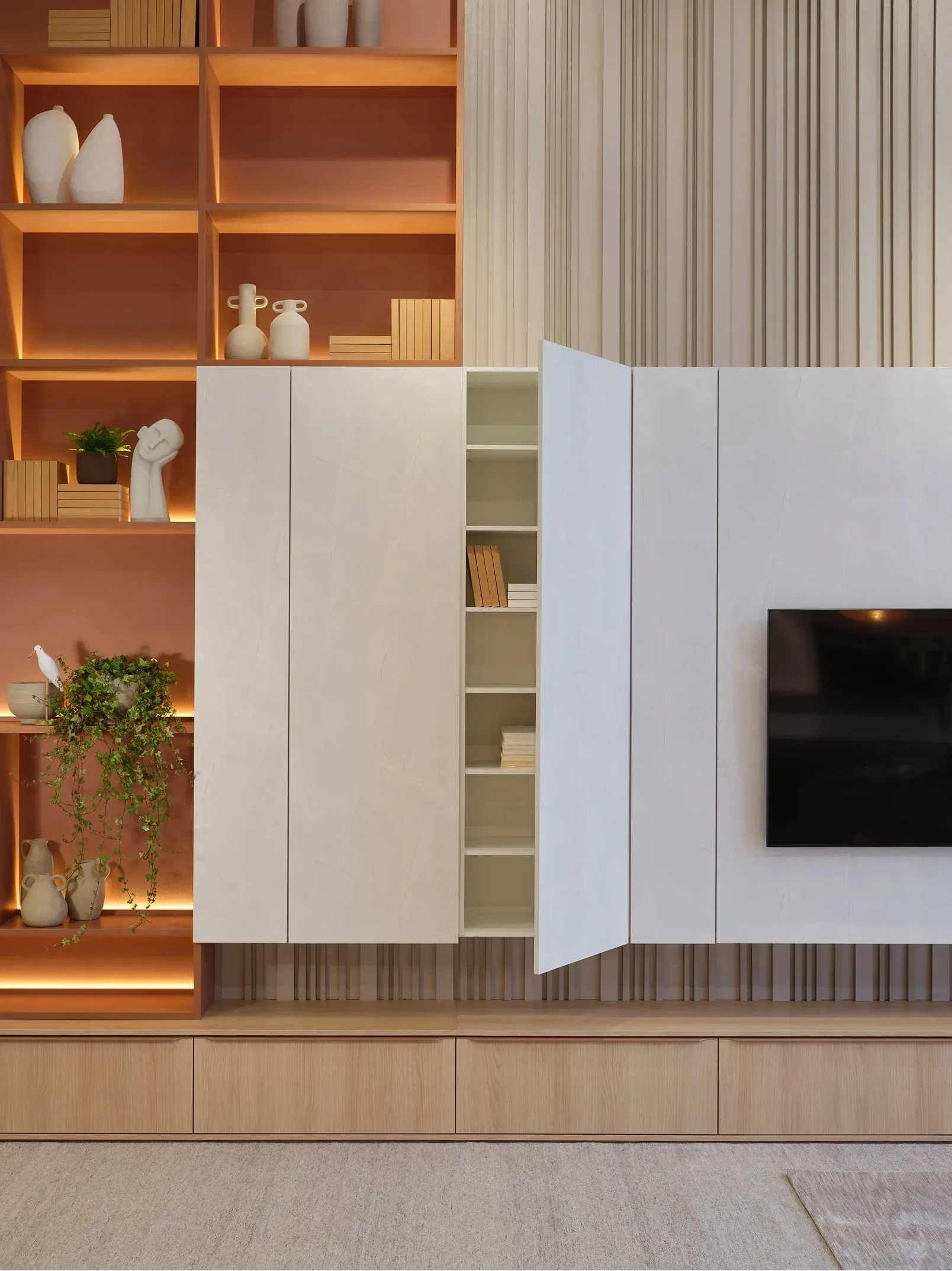 Pared moderna de la sala de estar con estantes de madera, gabinetes beige y un televisor montado en la pared.
