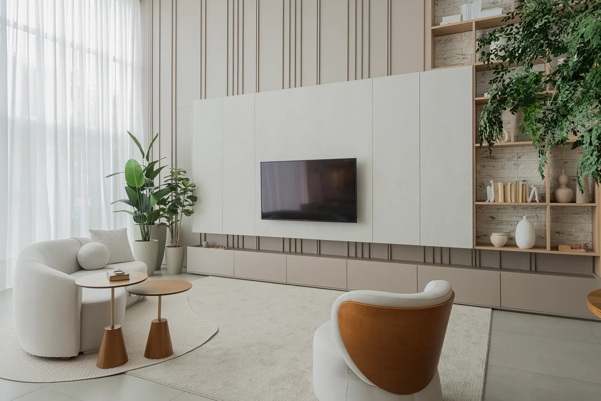 Salón moderno con paredes blancas, sillas curvas, televisor montado en la pared y plantas de interior altas.