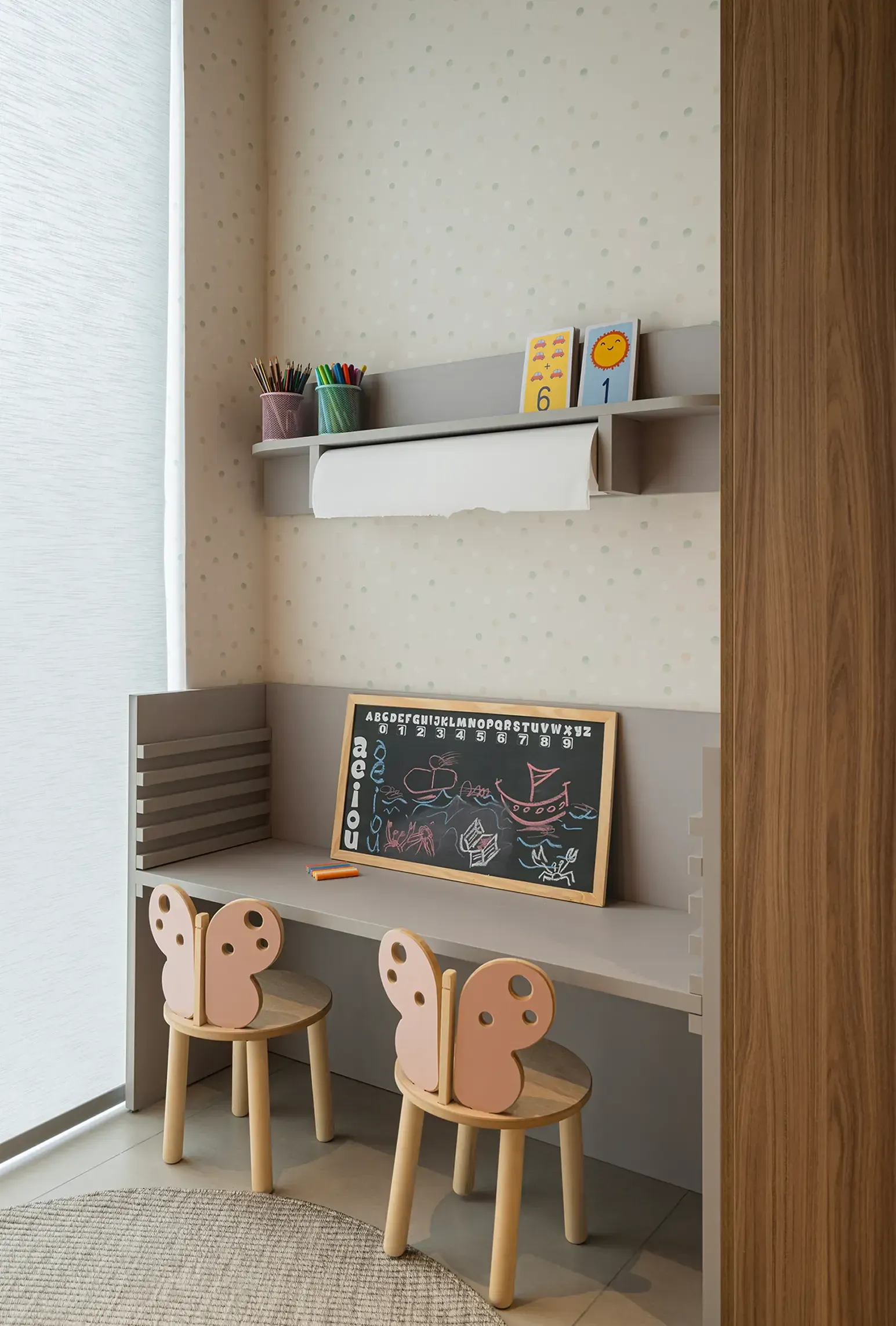 Escritorio infantil pequeño con dos sillas, pizarra y estantes de pared en un acogedor rincón de la sala de juegos.