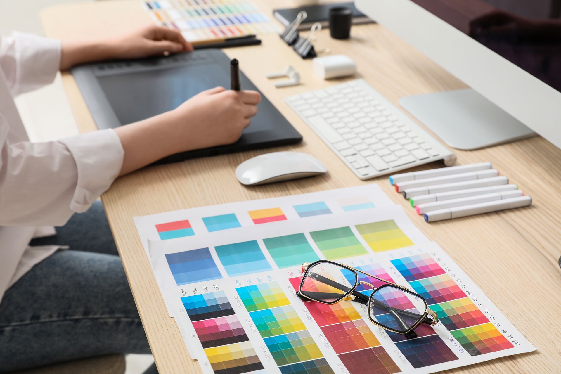 Designer revisando swatches de cores em uma mesa, utilizando um computador e uma mesa digitalizadora