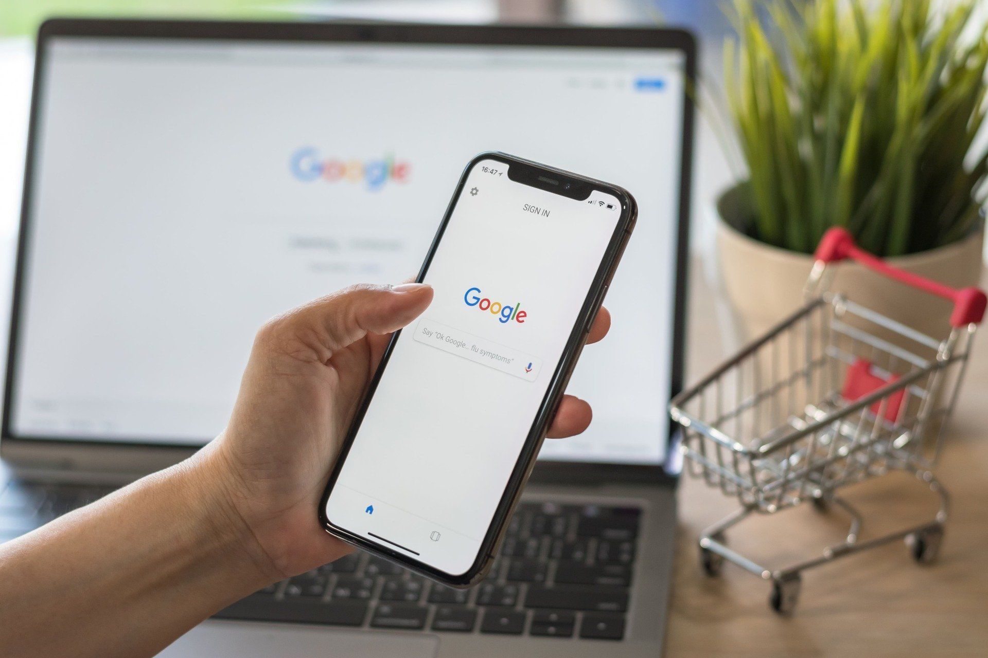 Uma pessoa está segurando um telefone celular na frente de um laptop e um carrinho de compras.