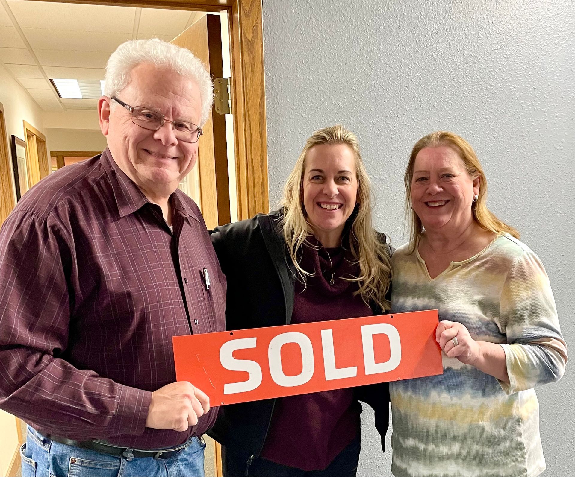 A man and two women are holding a sold sign in a room.