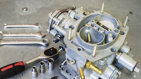 A close up of a carburetor with tools on a table.
