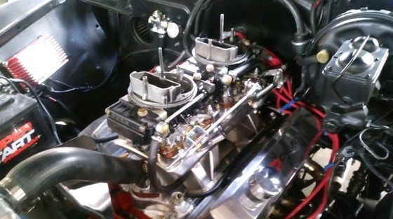 A close up of a car engine with a battery in the background