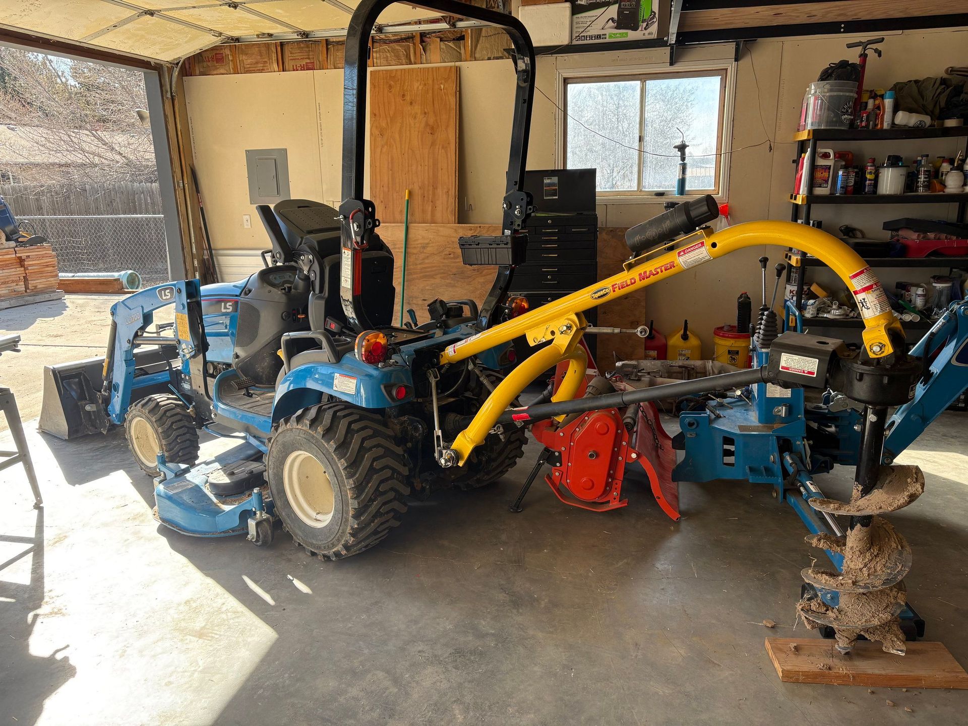 Blue tractor with yellow wood chipper in a garage workshop, with tools and equipment in the background