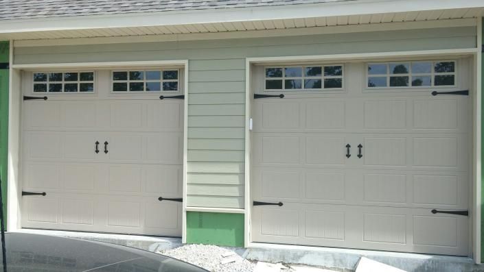 Two beige garage doors with small windows on a light green house exterior