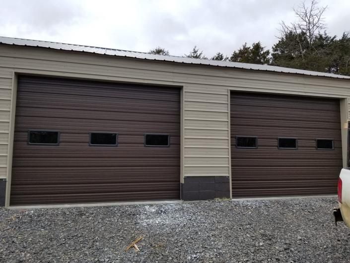 Two beige garage doors with brown trim on a gravel driveway, one partially visible vehicle at right