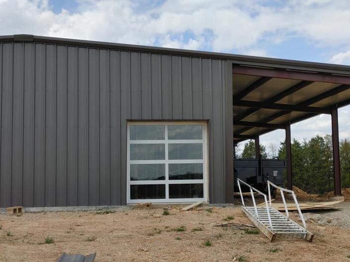 Gray metal warehouse with a large garage door and a small ramp entrance on a gravel lot