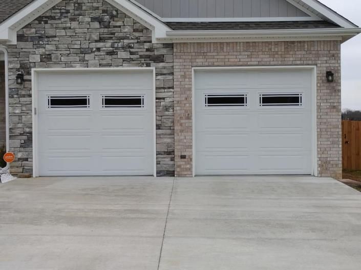 Front view of a house with two gray garage doors and a wide concrete driveway