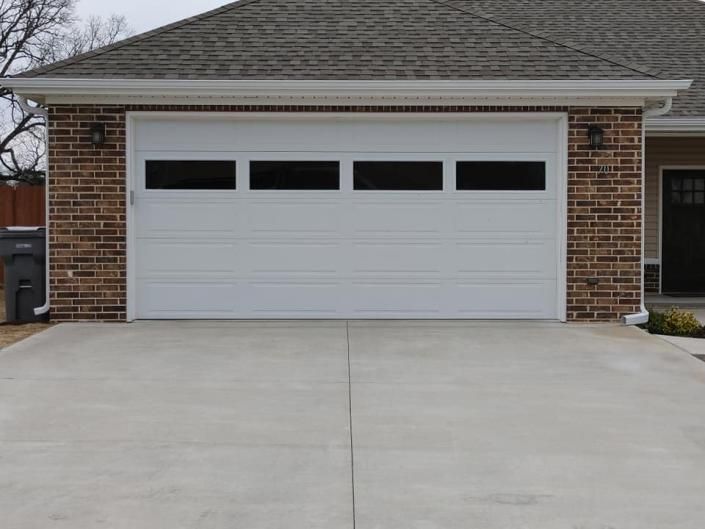 White garage door on a brick house with a concrete driveway under an overcast sky