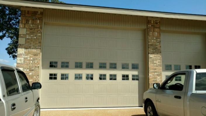 Two white pickup trucks parked outside a beige garage with two closed roll-up doors