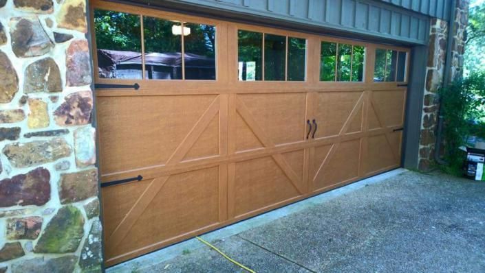 Closed tan garage door with windows at a stone house driveway