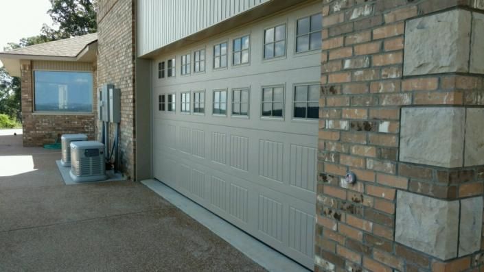 Closed garage door on a brick building beside a concrete driveway, with windows above and a side entry door.