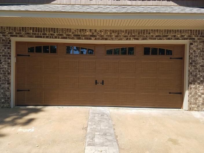 Tan garage door with small windows on a stone-sided house, viewed from a driveway