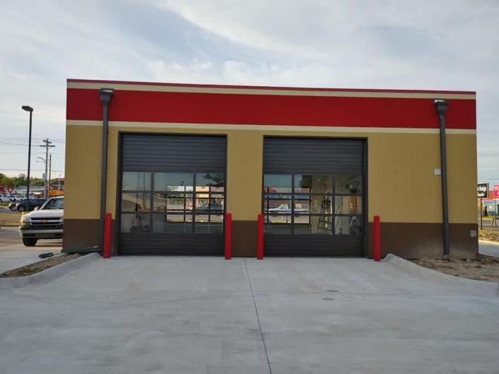 Tan building with red trim and two closed garage doors facing a concrete lot