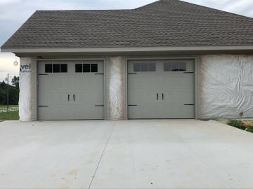 Two-car garage with gray doors and a wide concrete driveway, front view of a house under construction