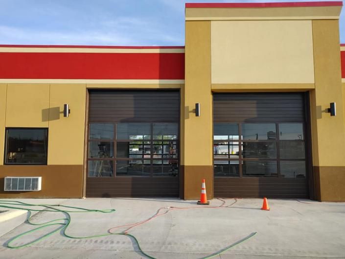 Empty storefront with two large garage doors, beige and red facade, and orange safety cones in front