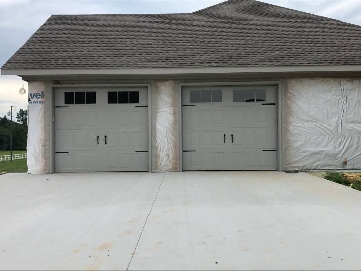 Two-car garage with gray doors and a concrete driveway in front of a house under construction