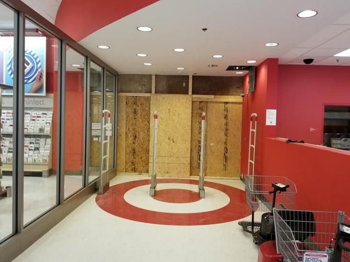 Empty storefront with red-and-white floor, glass walls, and boarded-up entrance inside a mall.