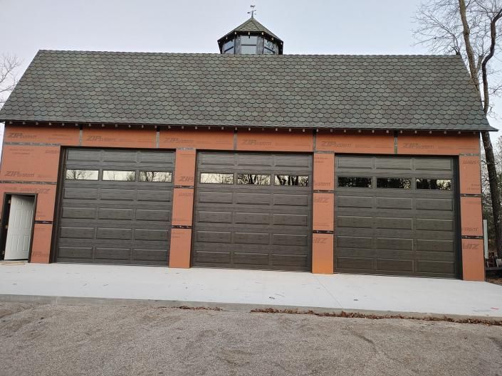 Three-car garage with dark doors and a gray shingled roof on a red-brick building