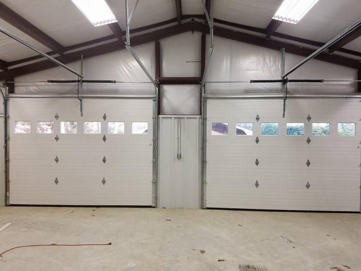 Interior of a garage with two white roll-up doors and exposed steel beams on a concrete floor