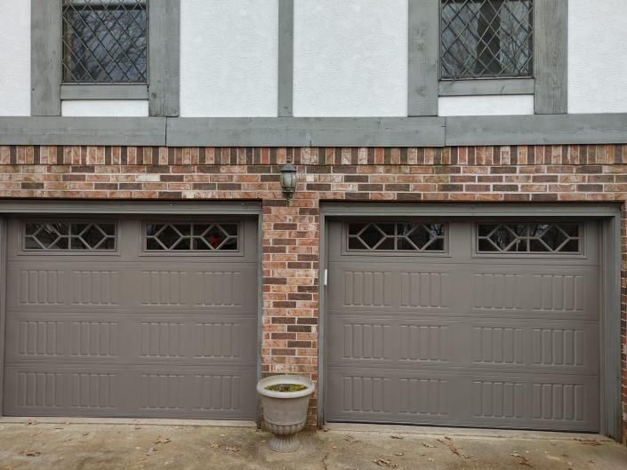 Two gray garage doors beneath a brick facade with a small planter centered between them.