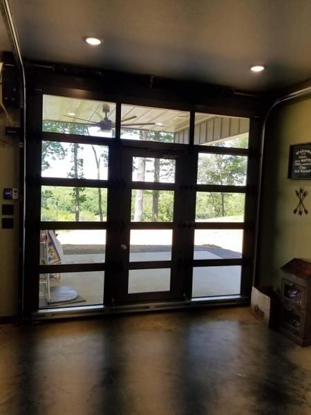 Glass double doors with dark frames opening to a bright outdoor patio and greenery beyond.