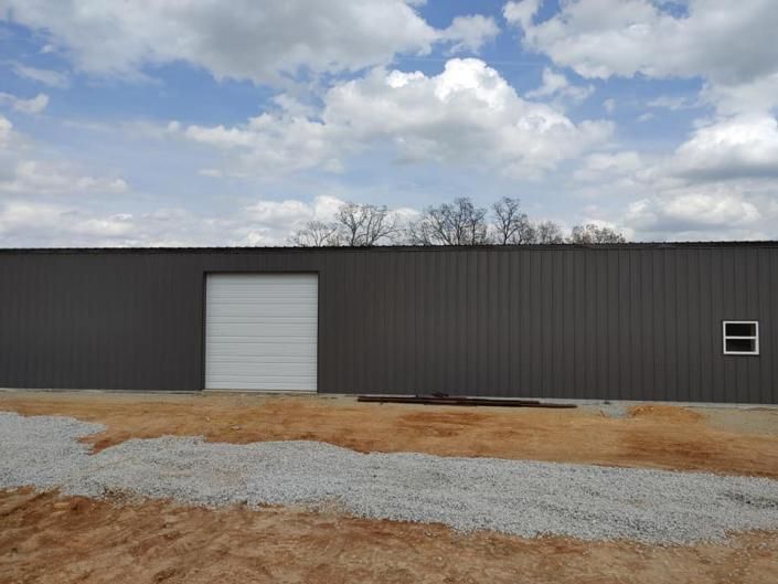 Long gray metal warehouse with a white roll-up door under a cloudy sky