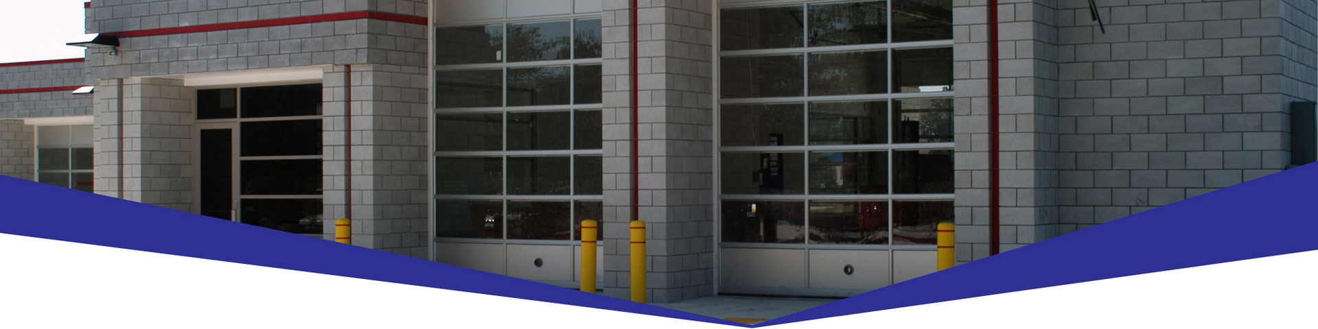 Entrance of a modern building with glass doors and windows, gray stone walls, and blue curved barriers in front