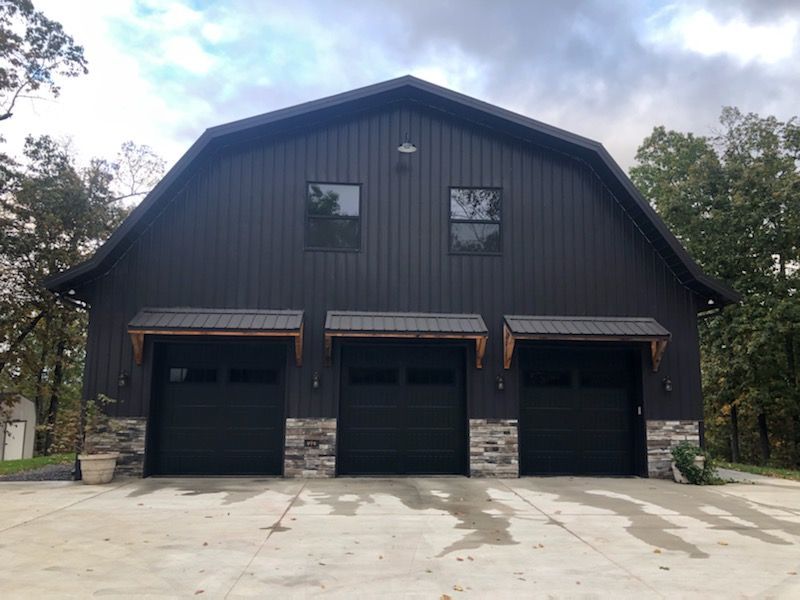 Dark two-story barn-style house with three black garage doors and stone accents on a concrete driveway