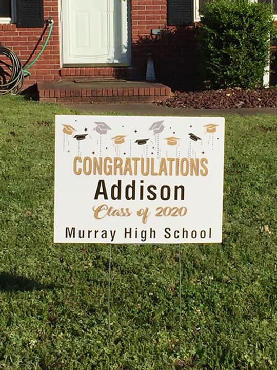yard sign is in the grass in front of a brick house.