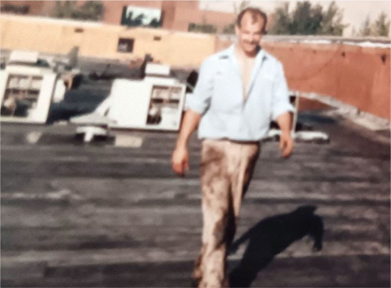 Man walking across a rooftop beside an airplane, wearing a light shirt and brown pants.